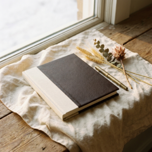 A premium hardcover book on cream linen with a brass pen and dried botanicals in warm golden light